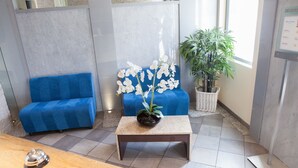 A reception area with a blue sofa, a small table with a potted orchid, and a bamboo plant. - Résidence La Villa d'Elsa (Antibes)