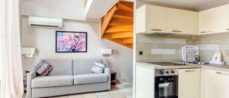 A compact living space with a kitchenette, a grey sofa, and a staircase.