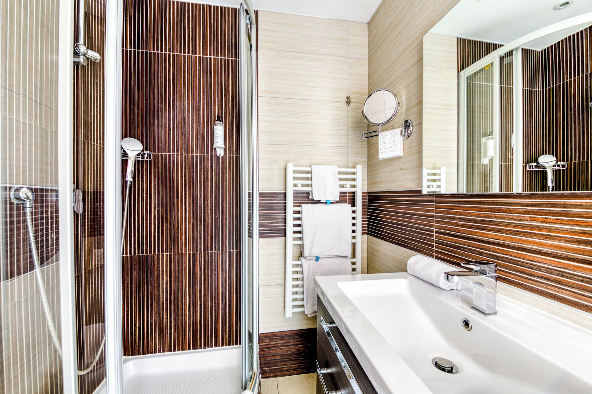 A modern bathroom with a walk-in shower, a large mirror, and a white sink.