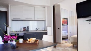 A modern hotel room with a dining area, kitchenette, and a TV mounted on the wall. - Résidence La Villa d'Elsa (Antibes)