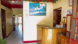 Zona de recepción con mostrador de madera, un cuadro enmarcado de una playa y un cartel que indica prohibido fumar.