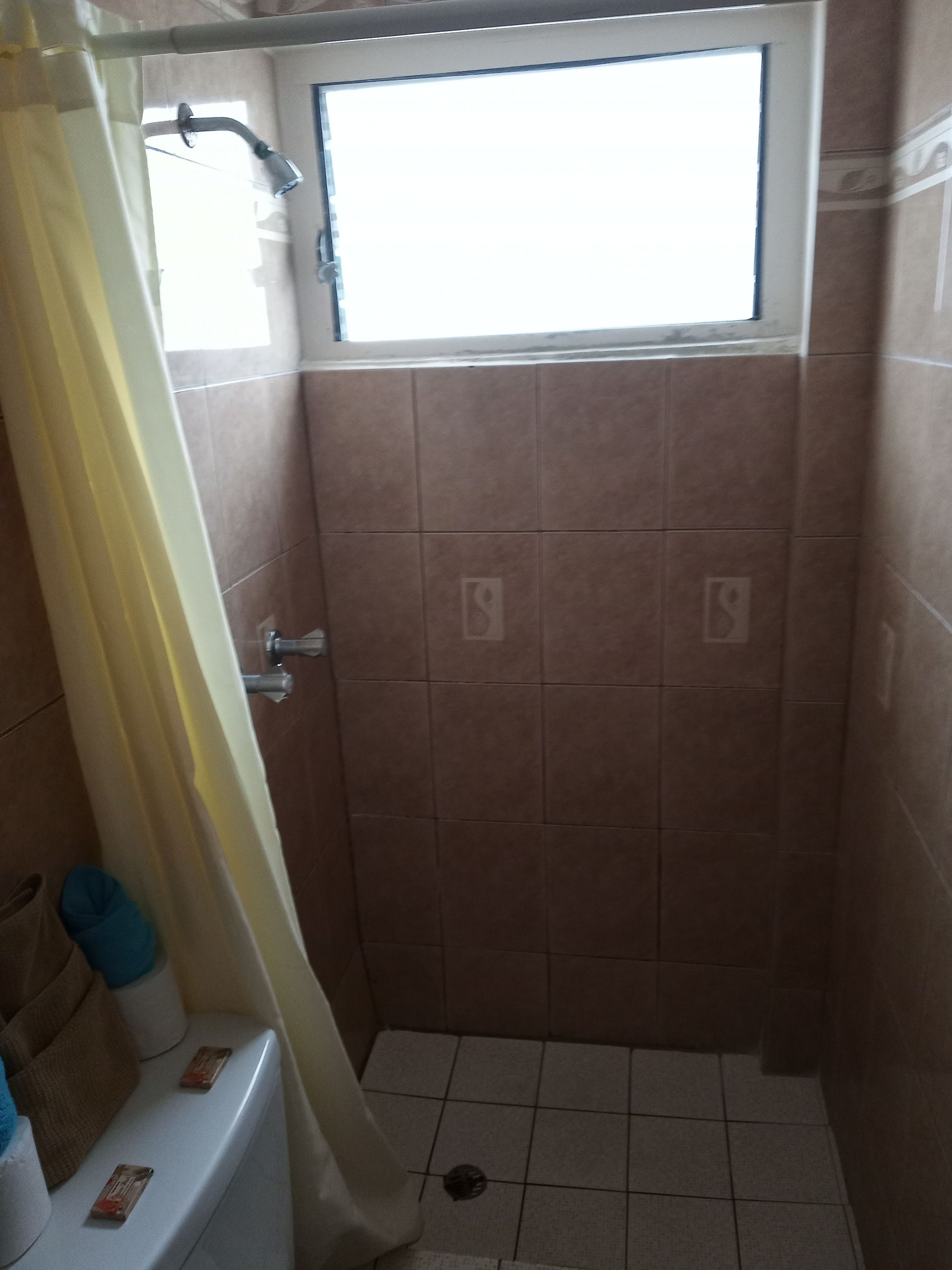 Un área de ducha pequeña y cerrada con paredes de azulejos y una ventana sobre la ducha.