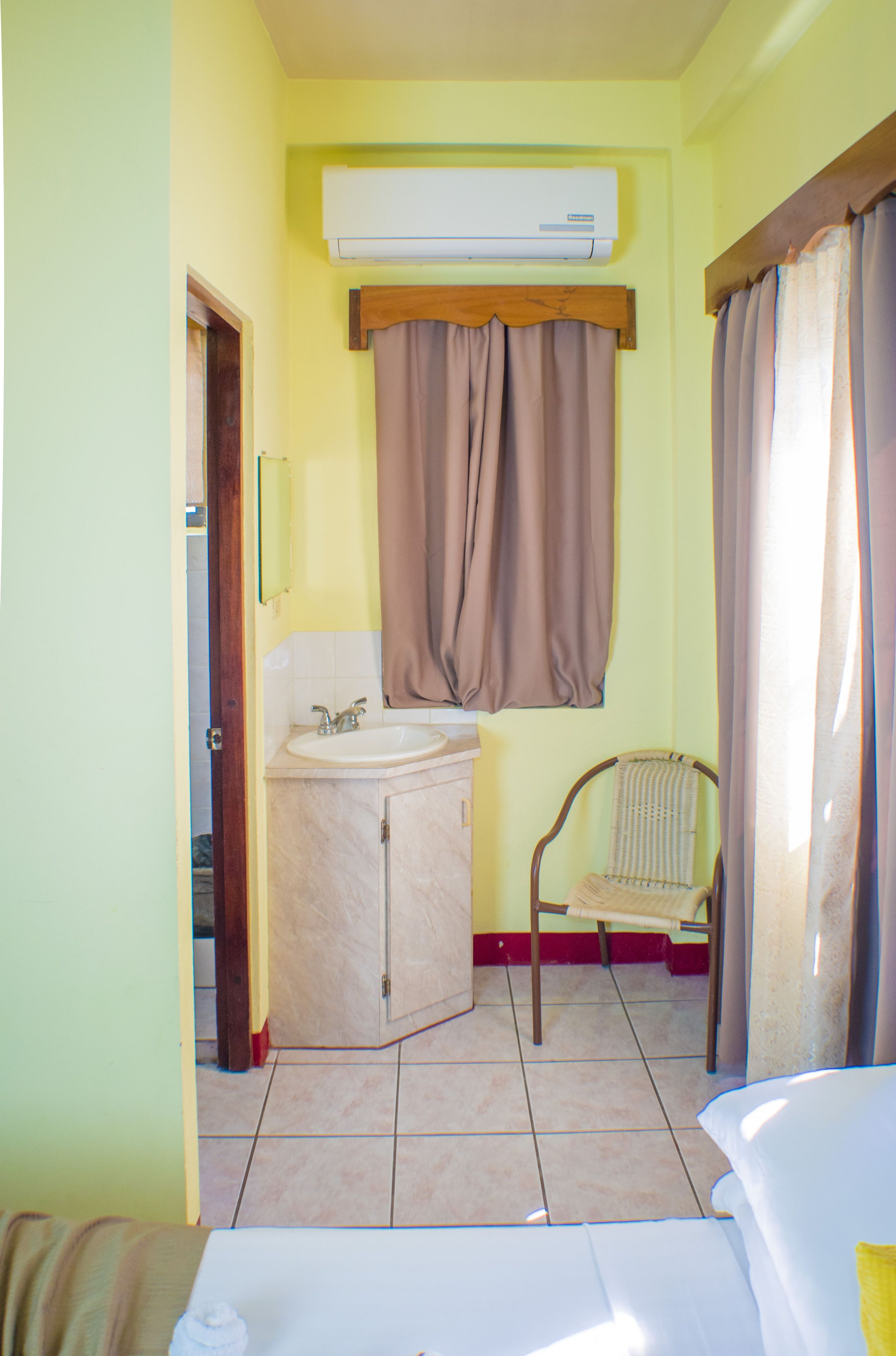 A small bathroom with a sink, mirror, and window with curtains.