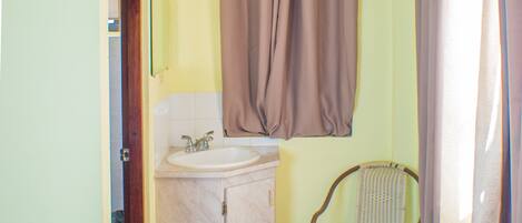 A small bathroom with a sink, mirror, and window with curtains.