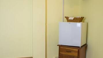 A hotel room with a bed, a small wooden table, a white refrigerator, and a television mounted on the wall.