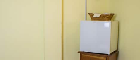 Una habitación de hotel con cama, una pequeña mesa de madera, un refrigerador blanco y un televisor montado en la pared.