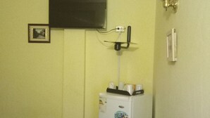 Una habitación con televisión montada en la pared, una mesita con una silla y un refrigerador.