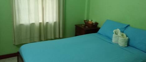 A room with a bed, a nightstand, a window with curtains, and a green wall.
