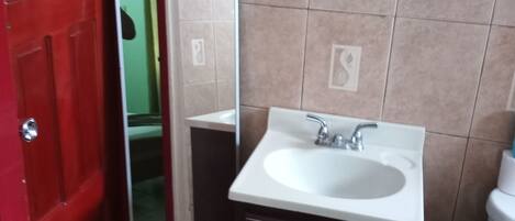 A bathroom with a white sink, dark cabinet, red door, and beige tiled walls.