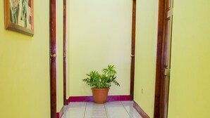 Un pasillo con paredes amarillas, suelo de baldosas y una planta en maceta en el centro.