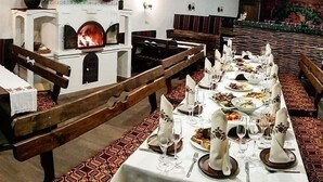 A restaurant with long communal tables set for dining, benches, and a fireplace. - Astoria (Chisinau)