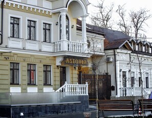 Un hôtel appelé ASTORIA, doté d’une façade classique, d’un balcon et d’une entrée fermée par un portail.