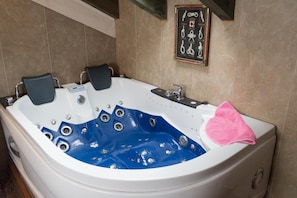 Un grand jacuzzi blanc et bleu, avec une serviette rose, une collection de clés encadrées et une étagère en bois au-dessus.