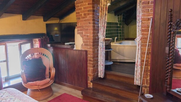 Ein gemütliches Zimmer mit Backsteinwand, einem Holzstuhl, einem Bett und einem Badezimmer mit Badewanne.