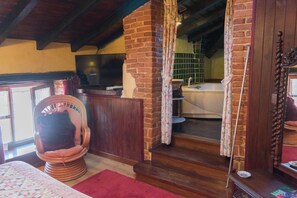 Une pièce chaleureuse avec un mur en briques, une chaise en bois, un lit et une salle de bain équipée d’une baignoire.