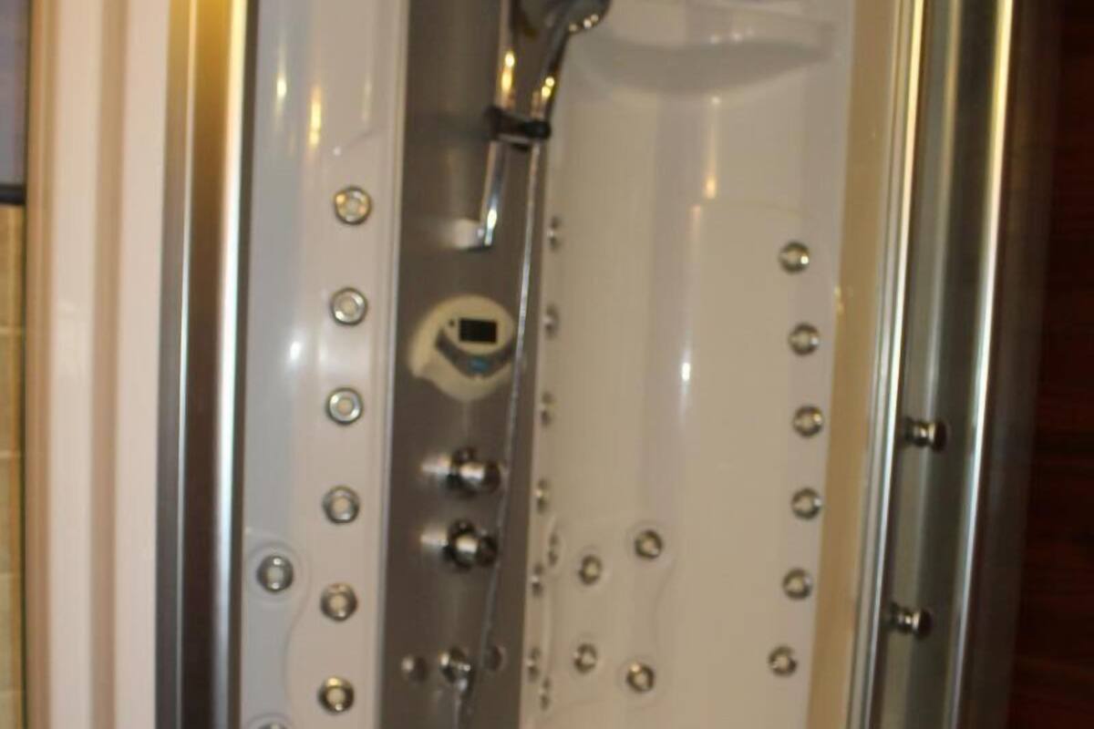 Une cabine de douche fermée par des parois en verre, dotée d’un pommeau de douche à main, d’un siège intégré et d’un panneau de commande avec des boutons.