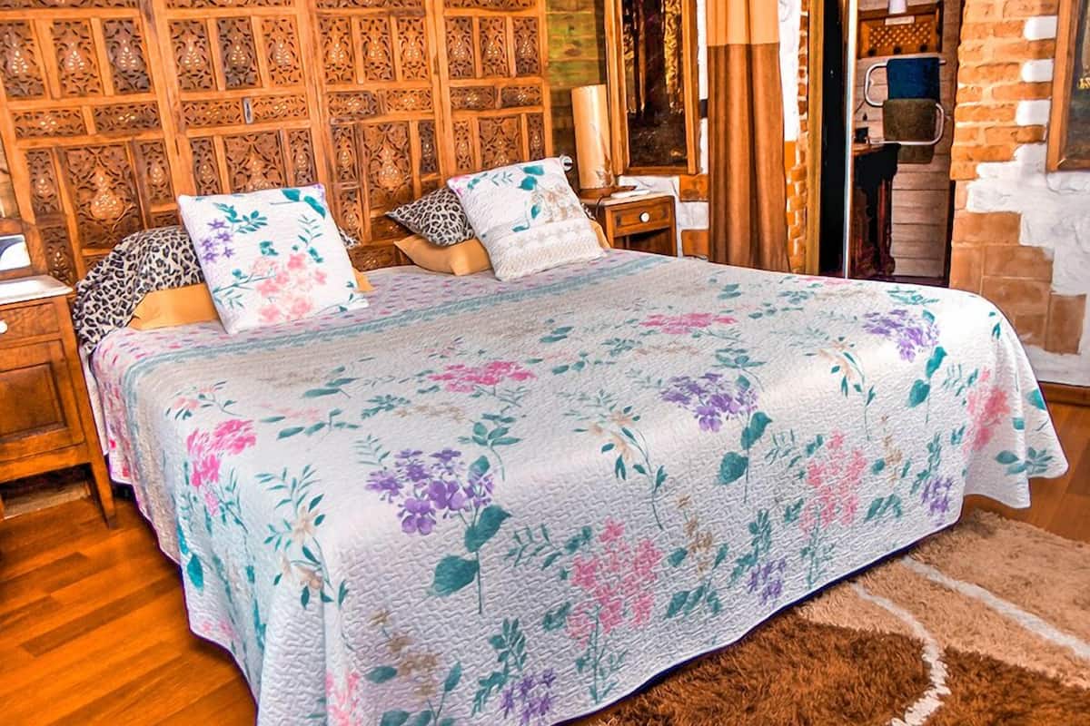 Ein Schlafzimmer mit einem blumigen Bettüberwurf, einem Holzkopfstück und einer Ziegelwand.