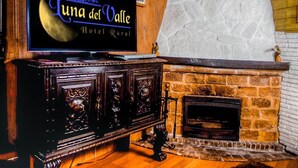Un televisore mostra 'Tuna del Valle Hotel Rural', con una parete in legno rustico e un camino in pietra.