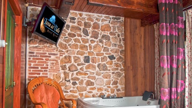 Un muro in pietra, una porta in legno, una sedia in vimini e una vasca idromassaggio bianca in una stanza.
