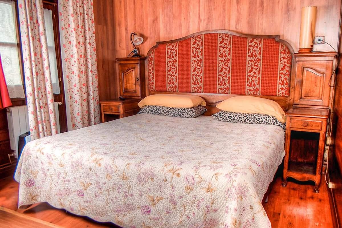 Ein Schlafzimmer mit floralem Bettbezug, einem Holzkopfteil, zwei Nachttischen und einem Beistelltisch.