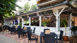 An outdoor cafe with tables and chairs, a menu board, and a potted plant. - CE Napfény Hotel (Siófok)