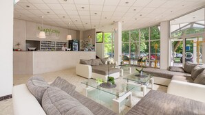 A hotel lobby with a reception desk, seating area, and large windows. - CE Napfény Hotel (Siófok)