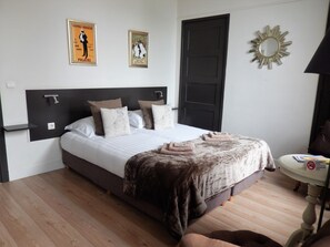 A neatly made bed with a black headboard, a small bedside table with a lamp, and two posters on the wall. - B&B de Passant (Breskens)