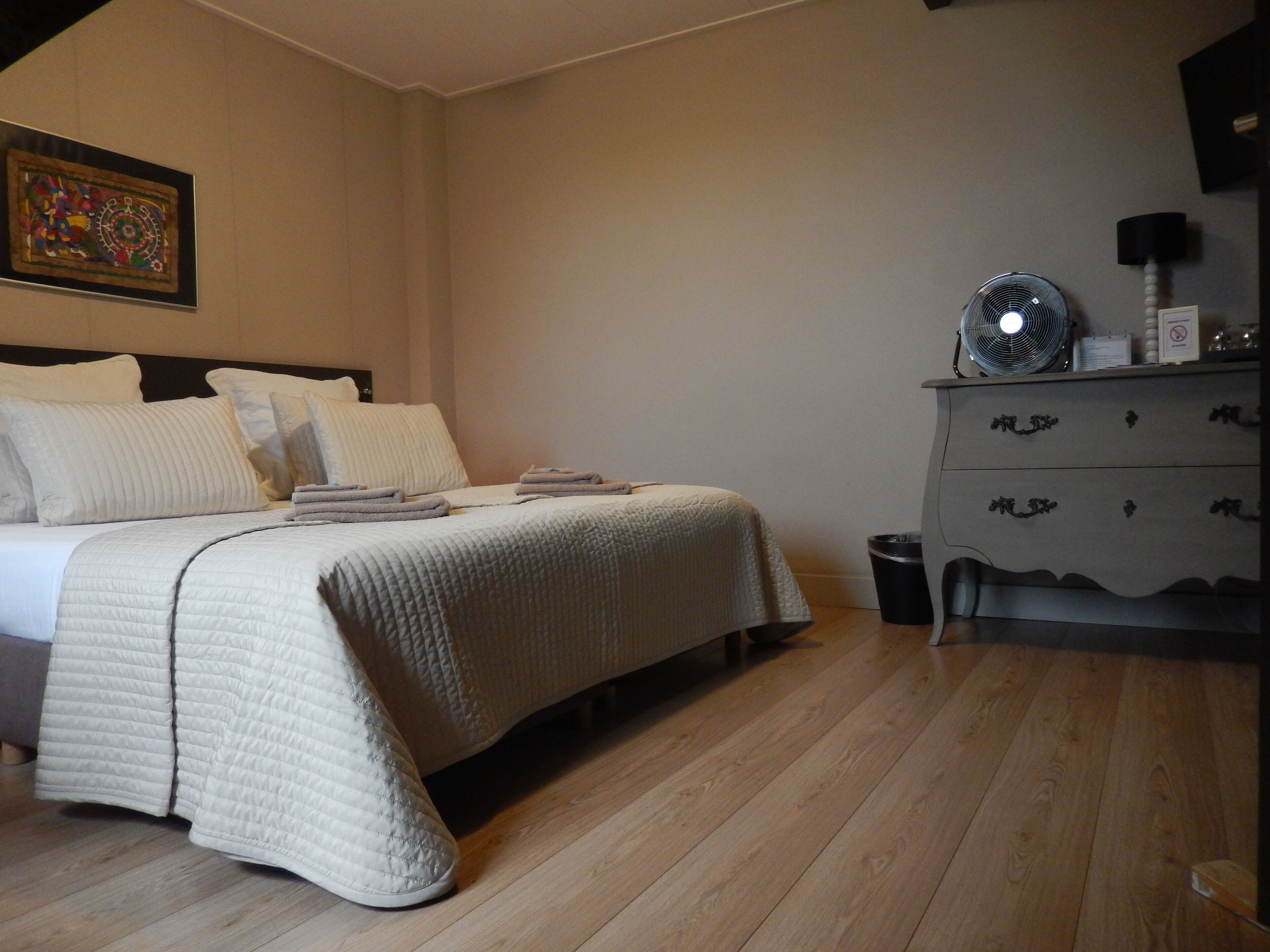 A bedroom with a bed, bedside table, dresser, and a wall-mounted fan.