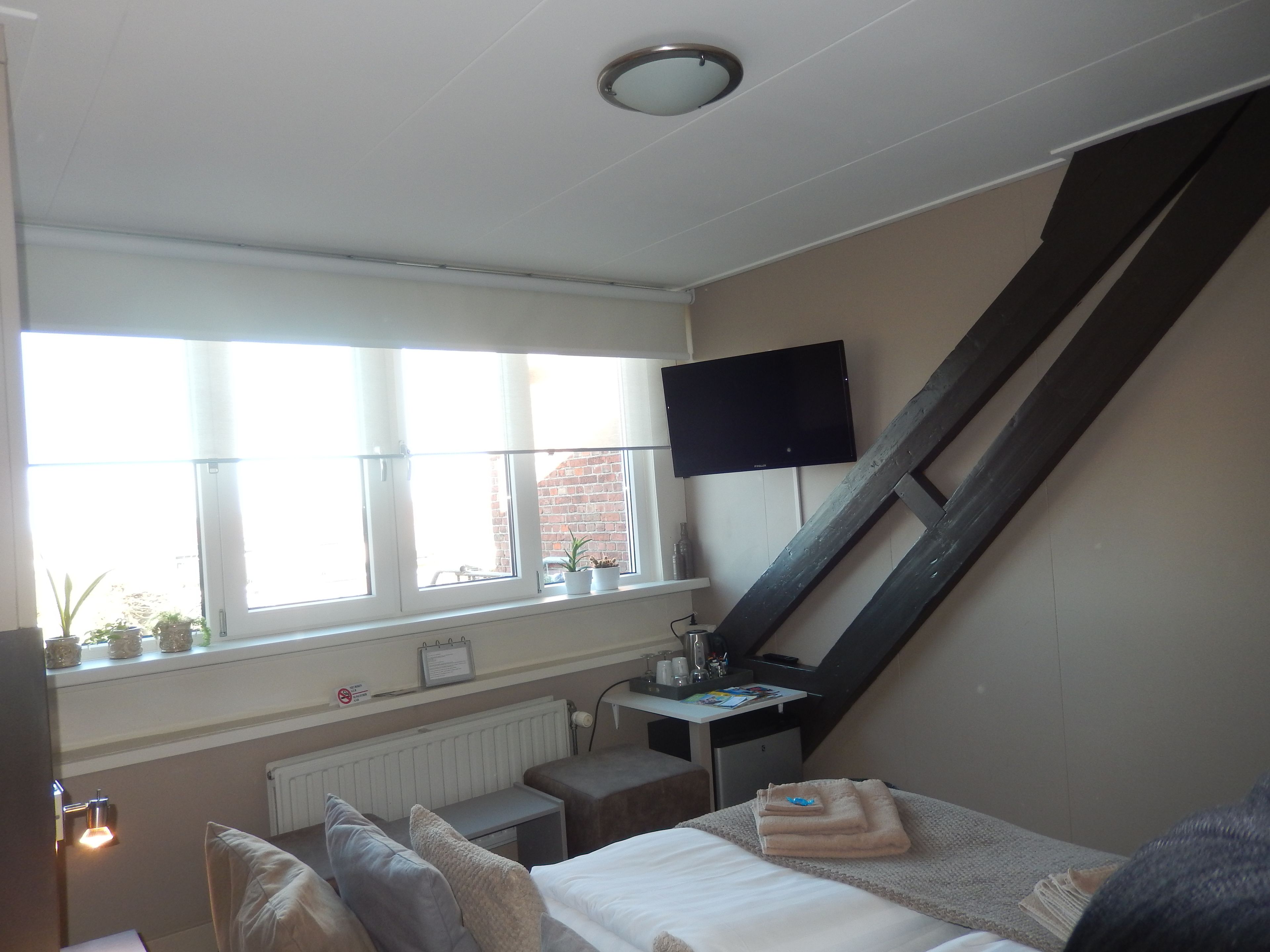 A bedroom with a bed, a desk, a chair, a TV, a window, and a radiator.