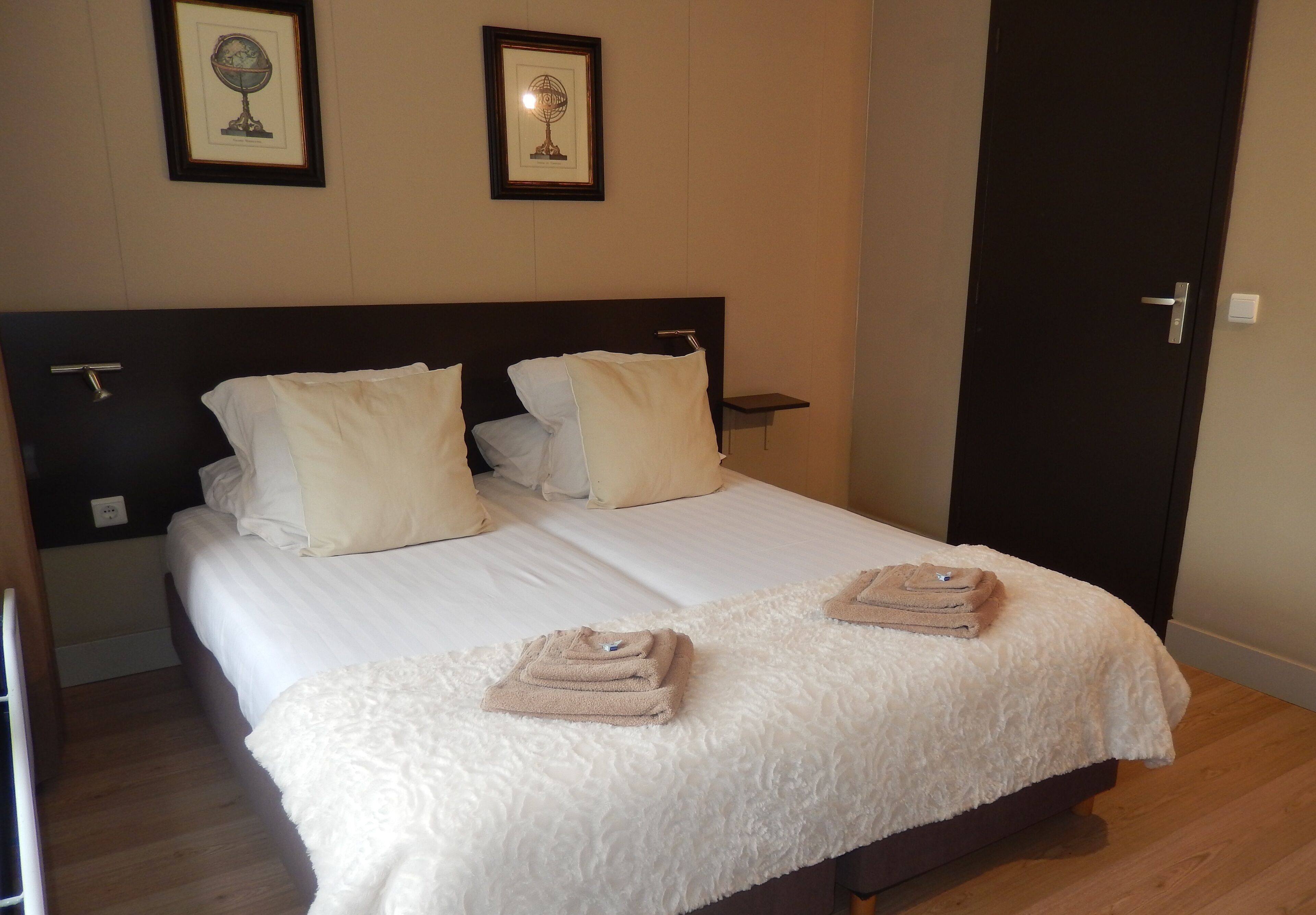 A neatly made bed with white linens, two pillows, and two folded towels on the bed.