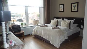 A bedroom with a large bed, a window with curtains, a bedside table with a lamp, and two framed pictures on the wall.