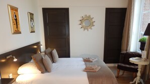 A neatly made bed with pillows and a blanket, a small table with a lamp, and a chair. - B&B de Passant (Breskens)