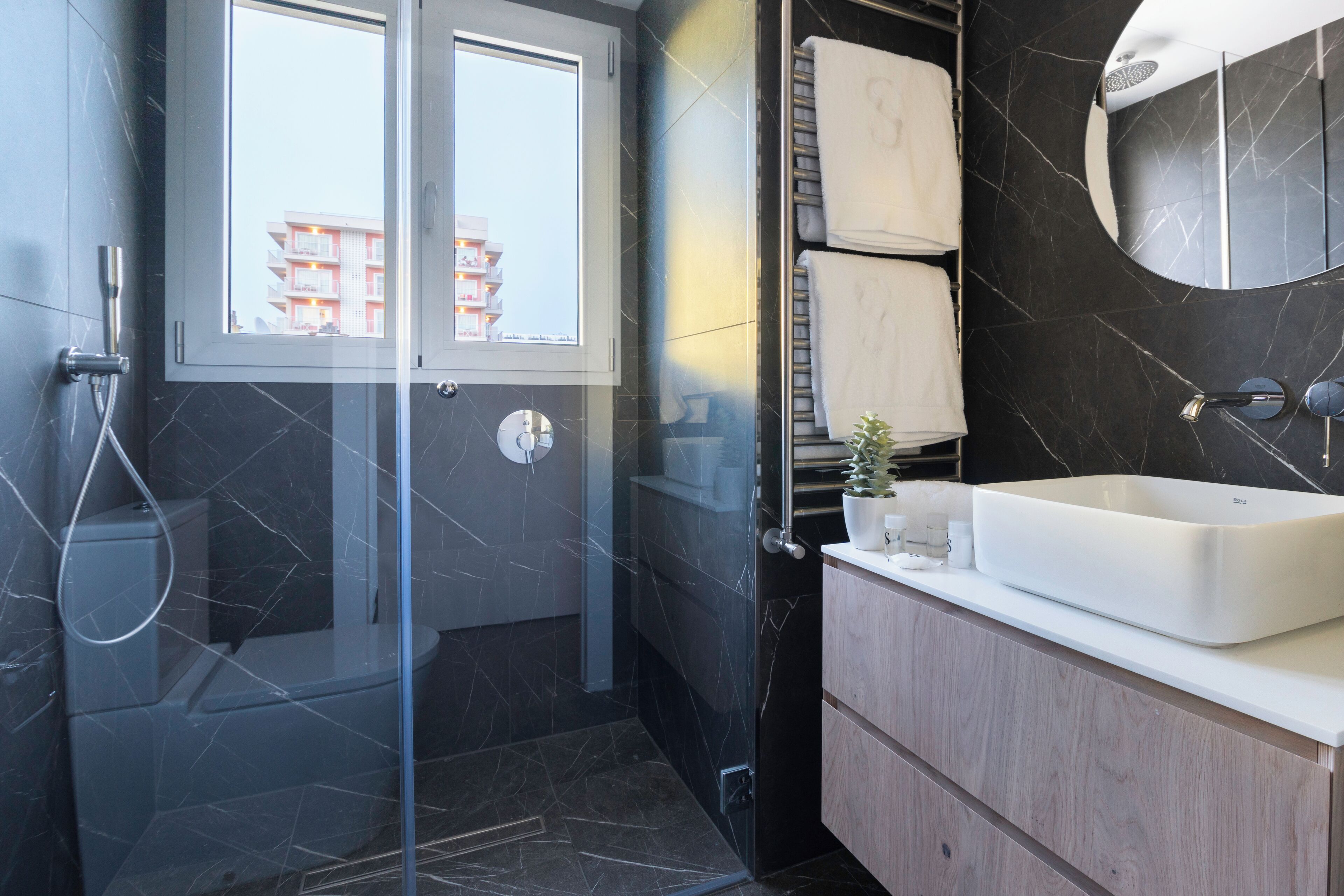 Un baño moderno con cabina de ducha de vidrio, lavamanos blanco y pared con azulejos oscuros.