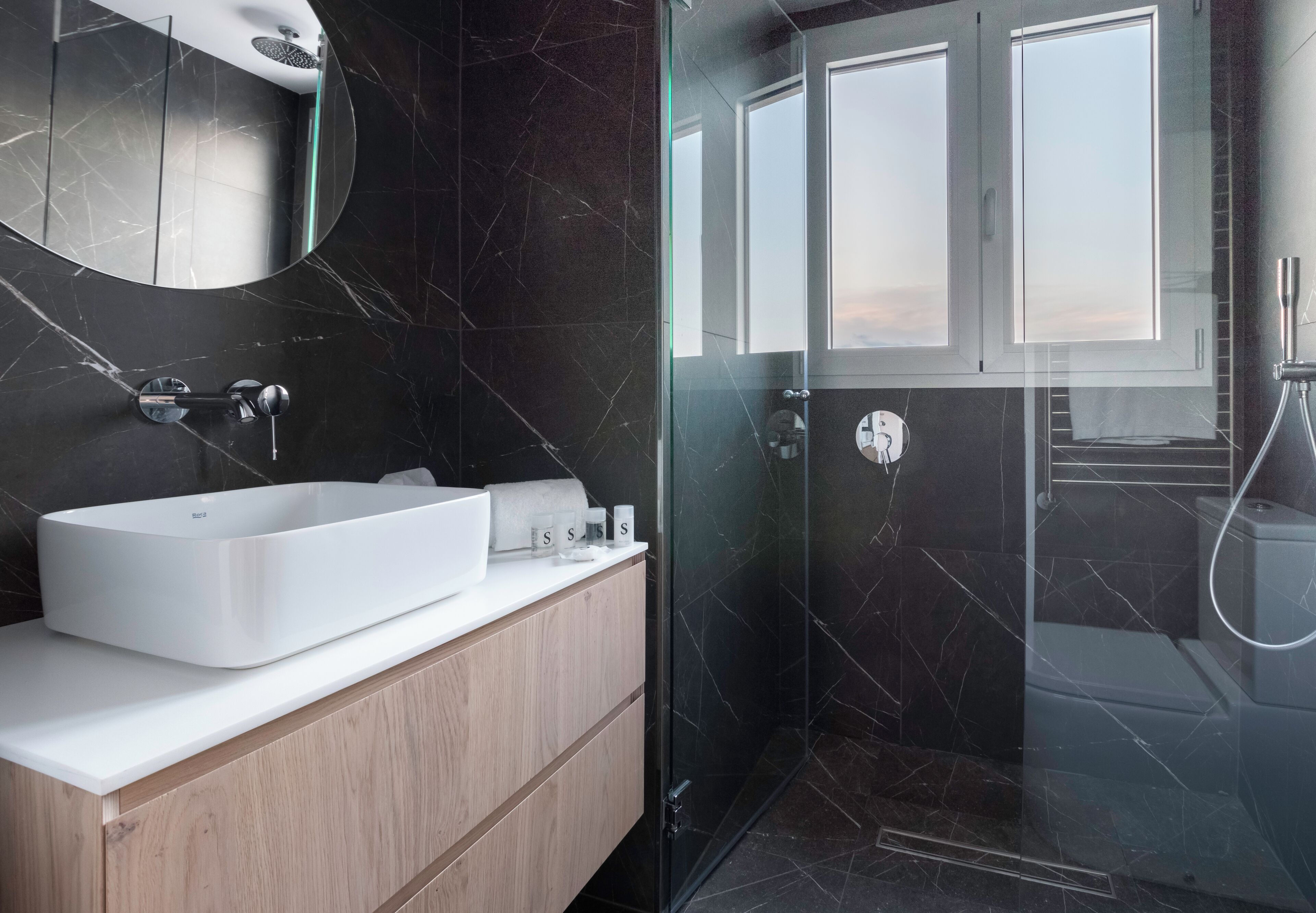 A modern bathroom with a large white sink, a wooden vanity, a glass shower enclosure, and a large mirror.
