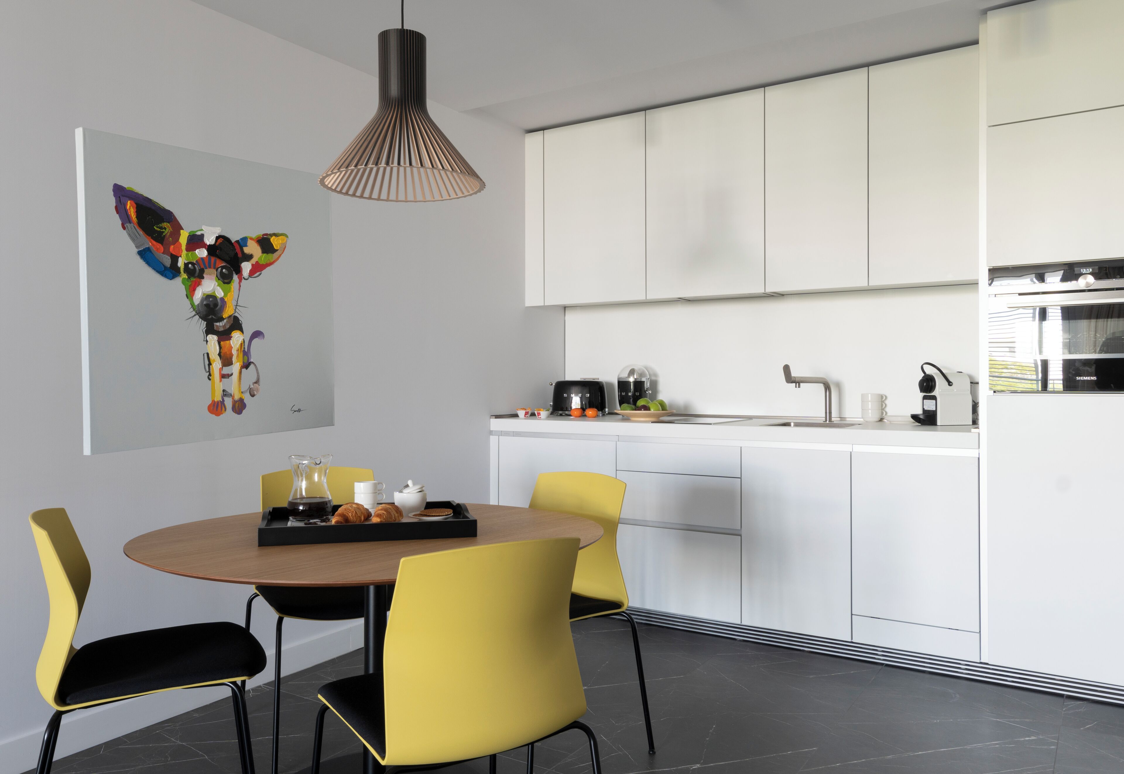 A modern kitchen with white cabinets, a dining area with yellow chairs, and a pendant light.