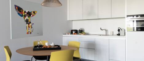 A modern kitchen with white cabinets, a dining area with yellow chairs, and a pendant light.