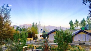 A campsite with tents and a wooden structure, surrounded by trees and mountains in the background. - D Camp (Leh)