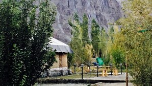 A rustic mountain lodge with a thatched-roof structure, surrounded by lush greenery and steep cliffs. - D Camp (Leh)