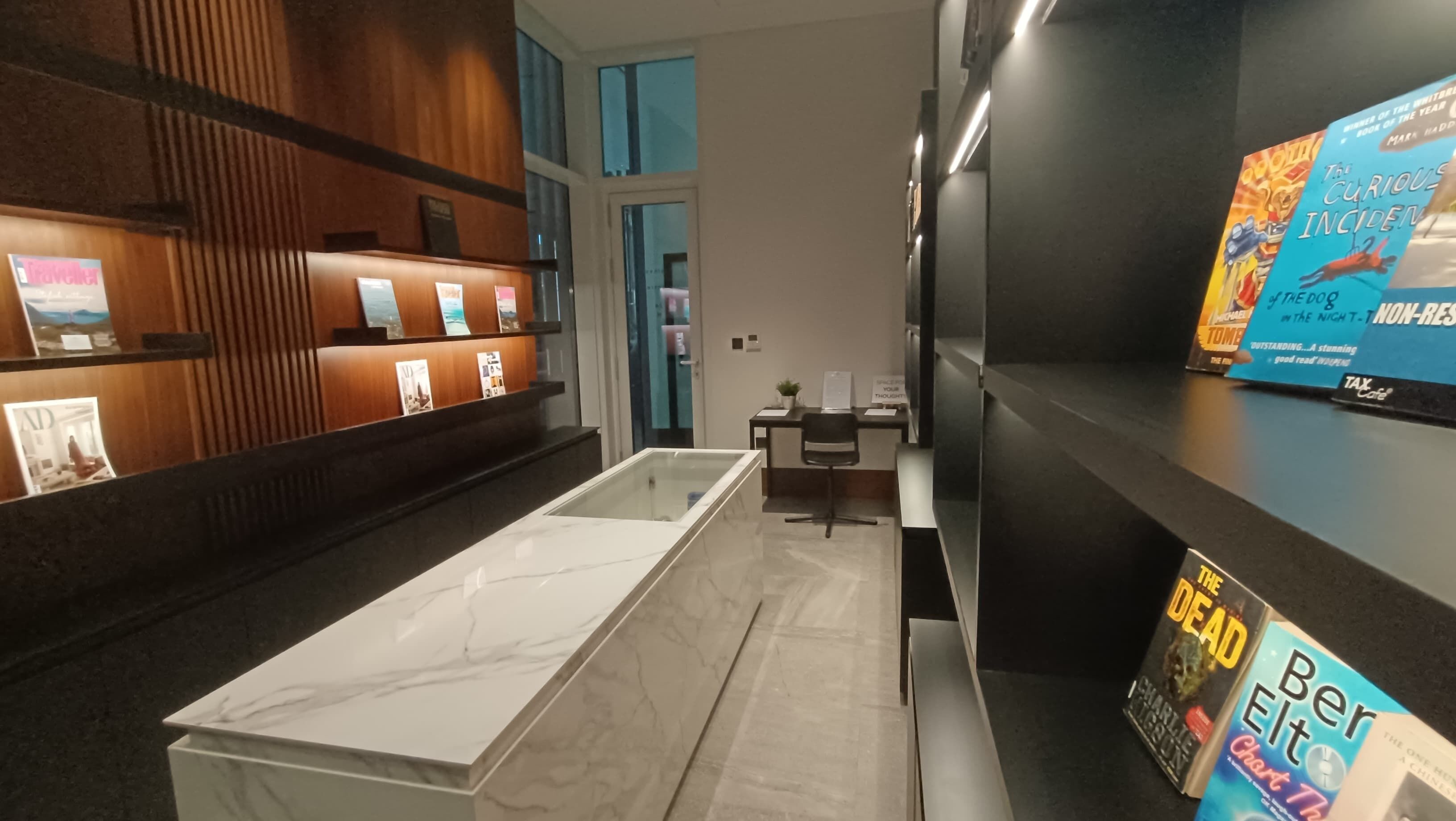 A modern hotel lobby with a marble reception desk, a wooden reception area with framed pictures, and a display of books on the right.