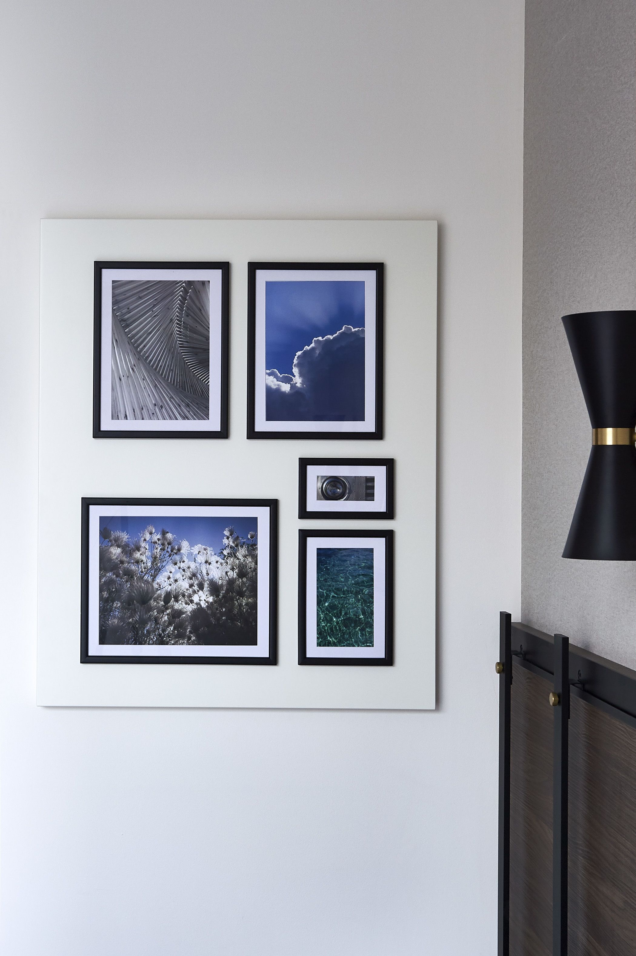 A wall with four framed pictures: a black and white abstract, a blue sky with clouds, a cactus landscape, and an underwater scene.