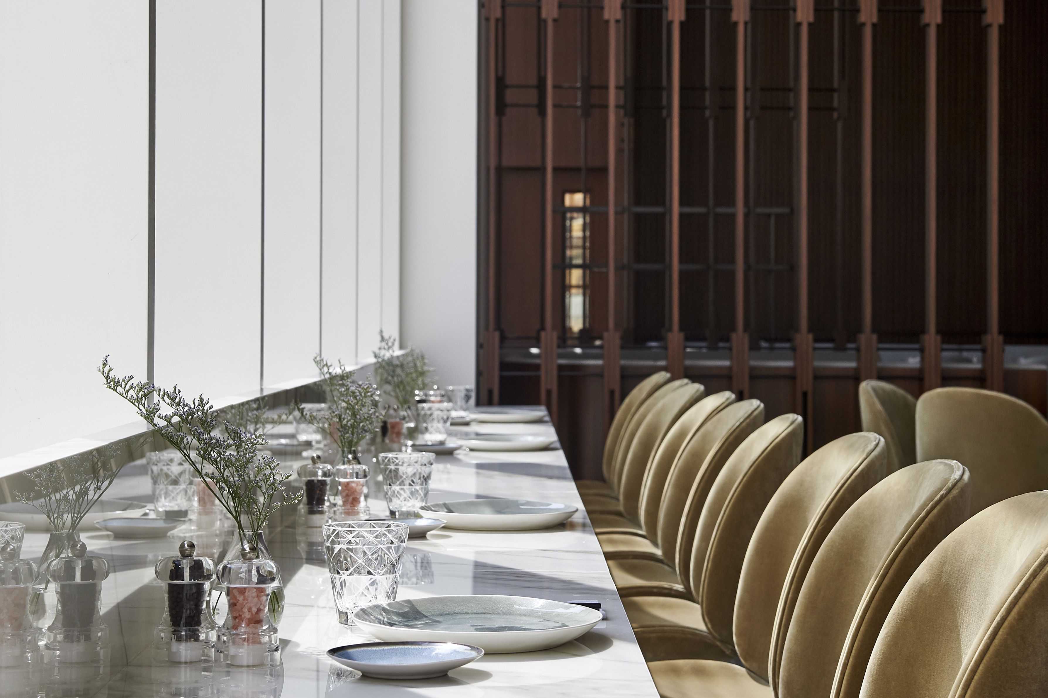 A long dining table set with plates, glasses, and decorative vases, flanked by rows of upholstered chairs.