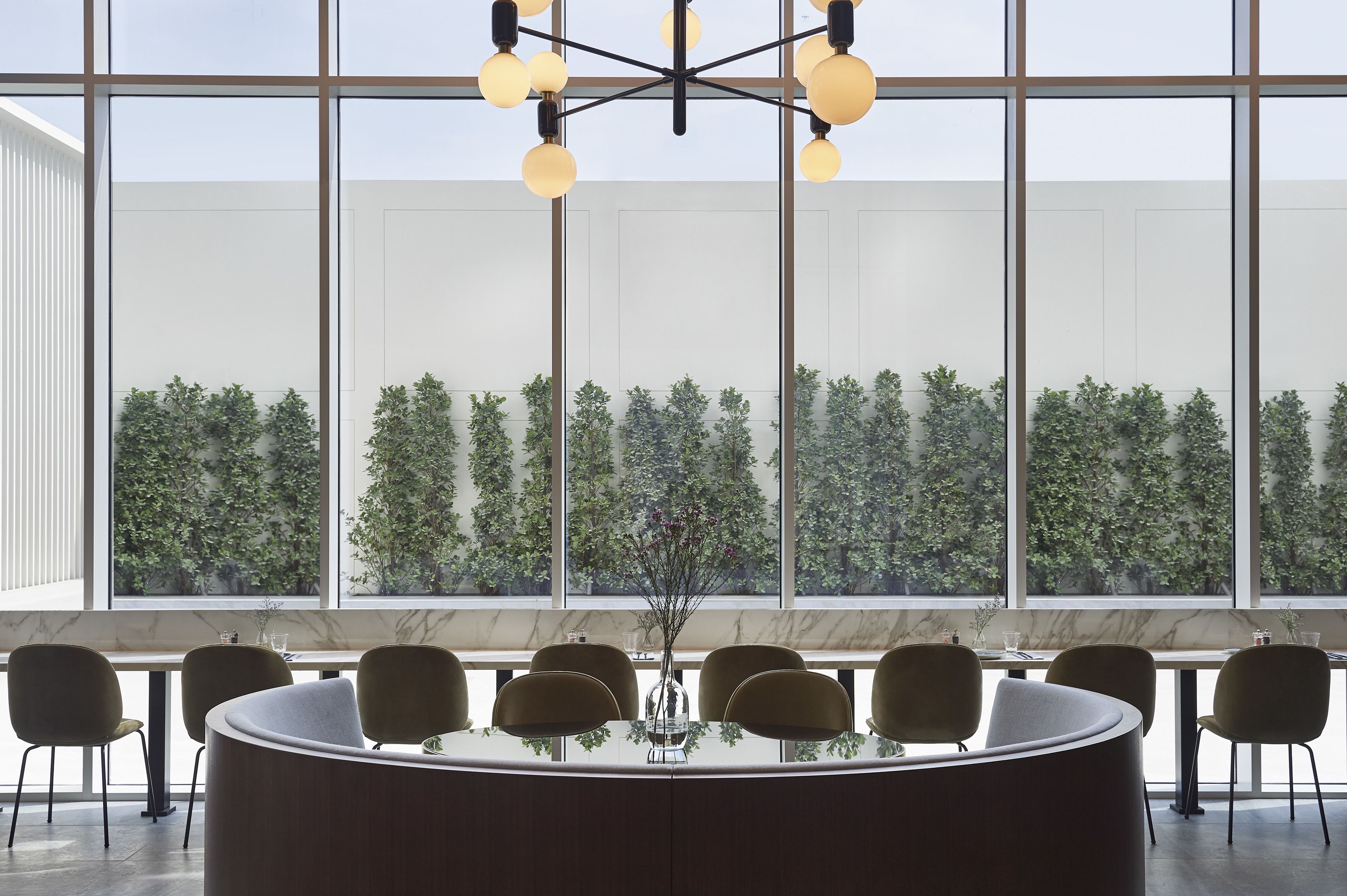 A modern conference room with a glass table, several chairs, and a large window with a view of a green garden.