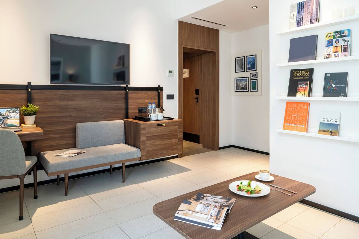 A modern waiting area with a sofa, a table with a meal, a TV, and a bookshelf with books.