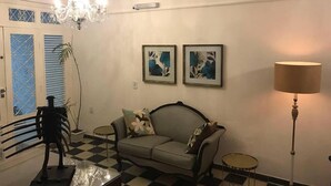 A living room with a checkered floor, a sofa, a chandelier, a lamp, and two framed pictures on the wall. - Hostel Pajuçara (Maceió)