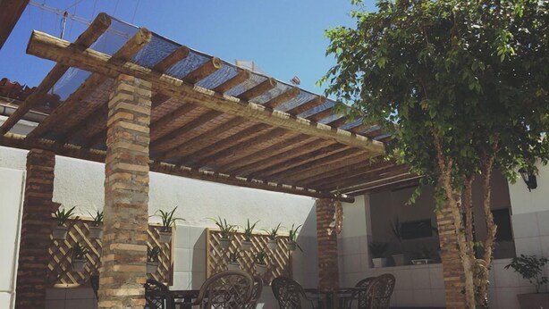 An outdoor patio with a pergola, brick columns, and a seating area with chairs and tables. - Hostel Pajuçara (Maceió)
