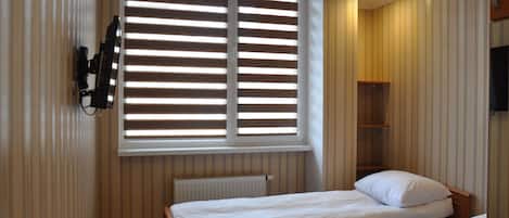 Un dormitorio con dos camas, una ventana con persianas, un radiador y un televisor montado.