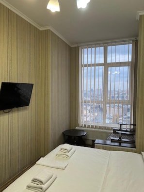 A hotel room with a large bed, a flat-screen TV mounted on the wall, a small round table, and a window with a city view. - Z-Apartments (Kyiv)