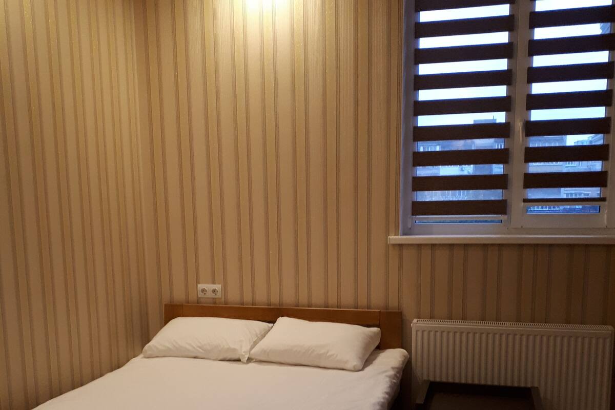A bedroom with a bed, a radiator, and a window with blinds.