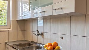 A kitchen with white cabinets, a stainless steel sink, and a bowl of fruit on the counter. - Apartments Stella del Mare (Risan)