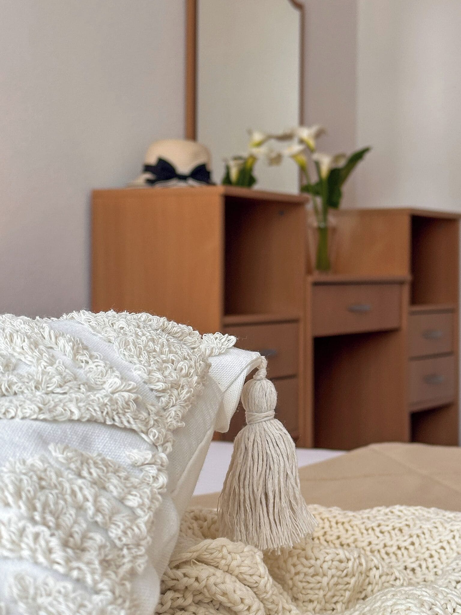 A bed with a white textured blanket and a beige knitted throw.